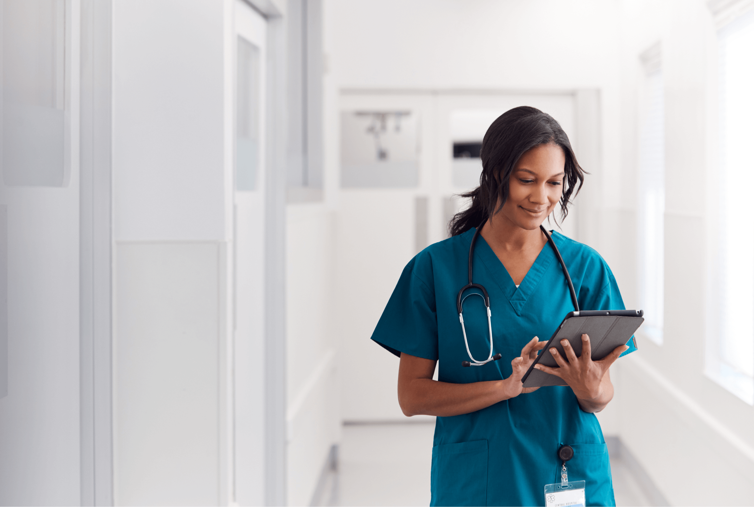 A female clinician uses a tablet in a white hospital corridor